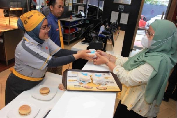 Karyawan sedang membagikan Chicken Muffin kepada pelanggan